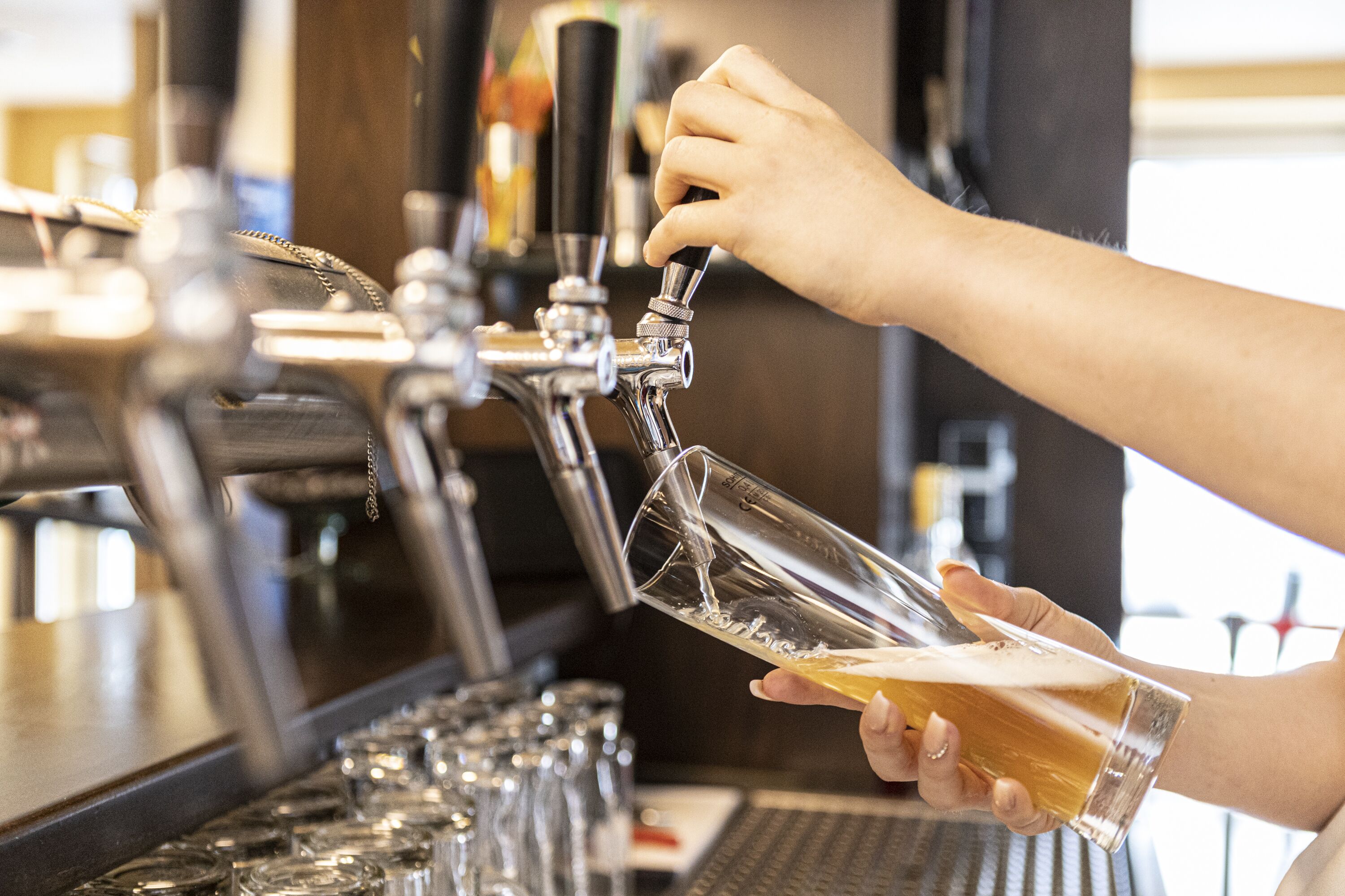 A hand pouring beer from a tap into a glass.