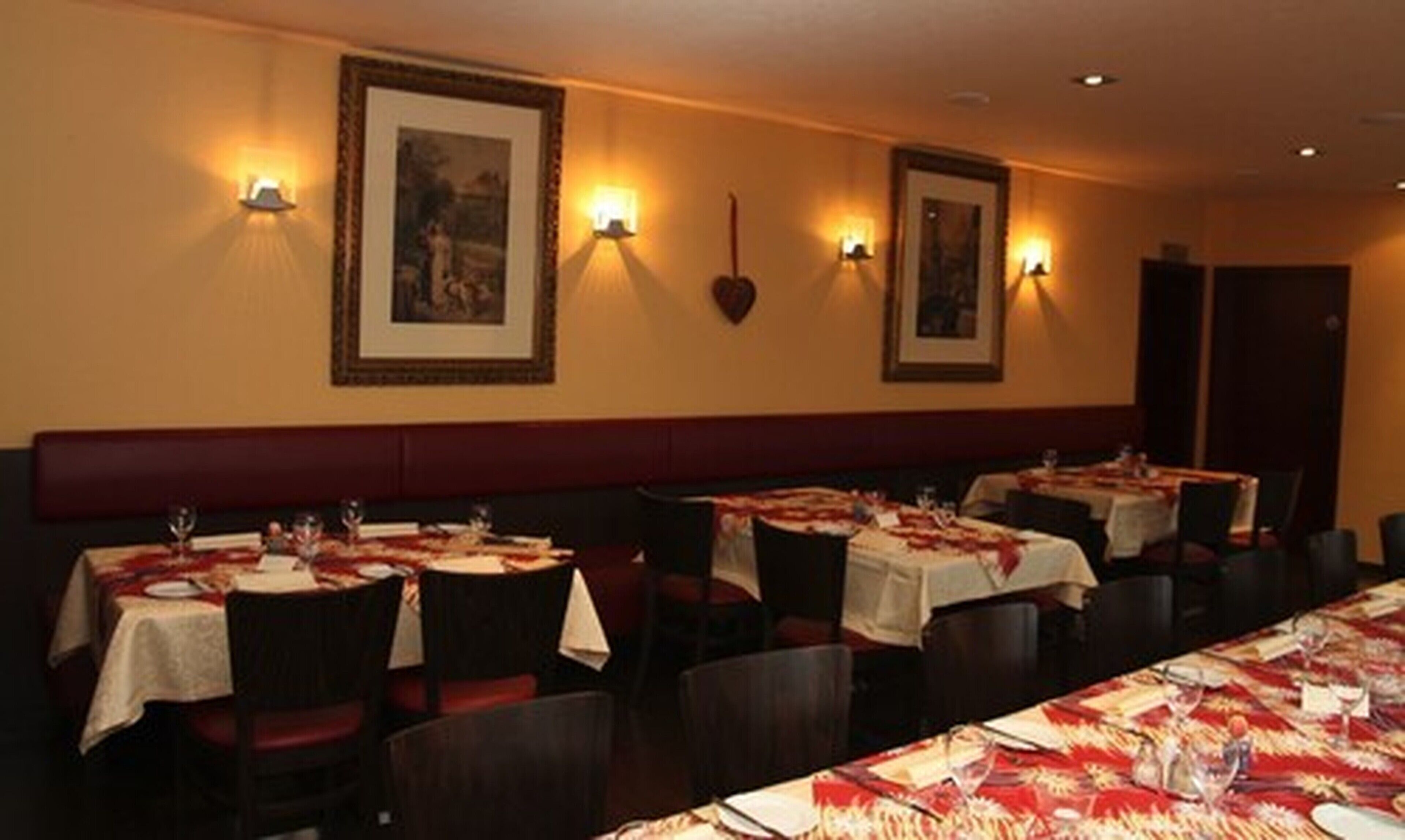 Un restaurante con varias mesas dispuestas para comer, cada una con mantel y copas de vino.