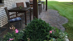 A patio with a brick wall, wooden furniture, and a garden with pink flowers. - Landhaus Pension Göke (Hoevelhof)