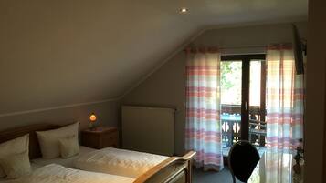 A bedroom with a bed, bedside lamp, and a view of the outside through a window with curtains.