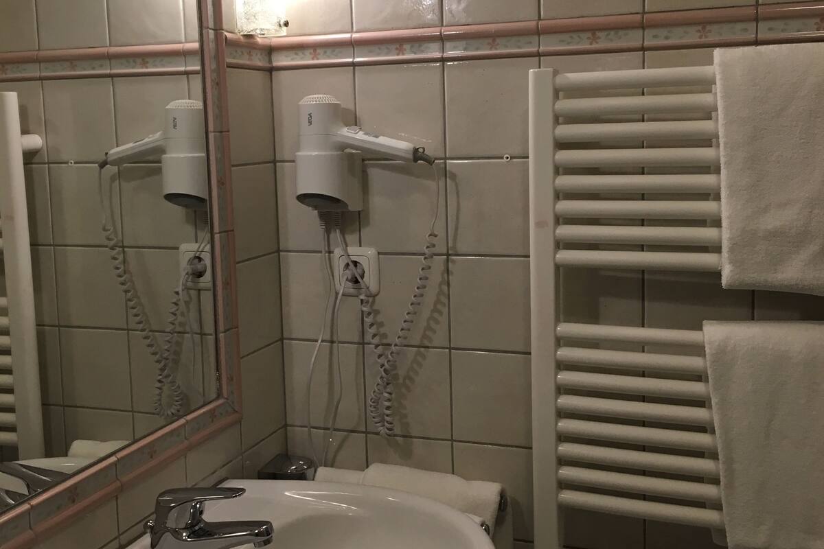 Une salle de bain équipée d’un lavabo, d’un miroir, d’un sèche-cheveux et d’un porte-serviettes.