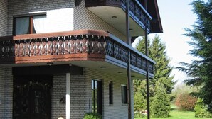 A two-story building with a red-tiled roof, a balcony with ornate railings, and a brick facade. - Landhaus Pension Göke (Hoevelhof)