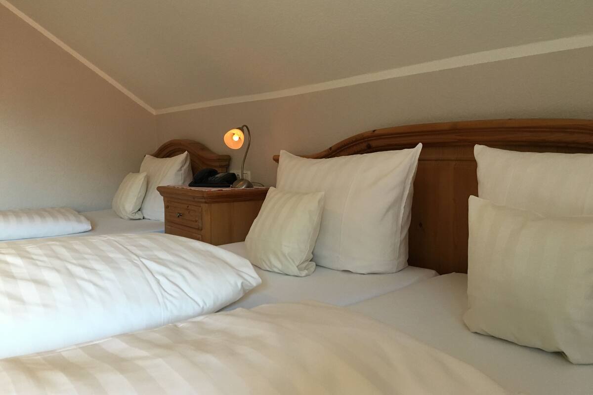 Une chambre d’hôtel avec deux lits, des têtes de lit en bois, du linge de lit blanc, une table de chevet avec une lampe et un téléphone.