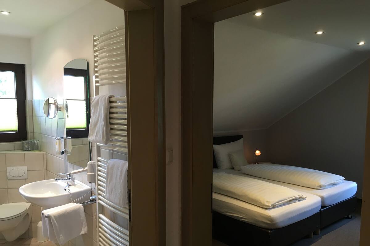 Une chambre moderne avec un lit, une table de chevet et une salle de bain équipée d’un lavabo et d’un miroir.