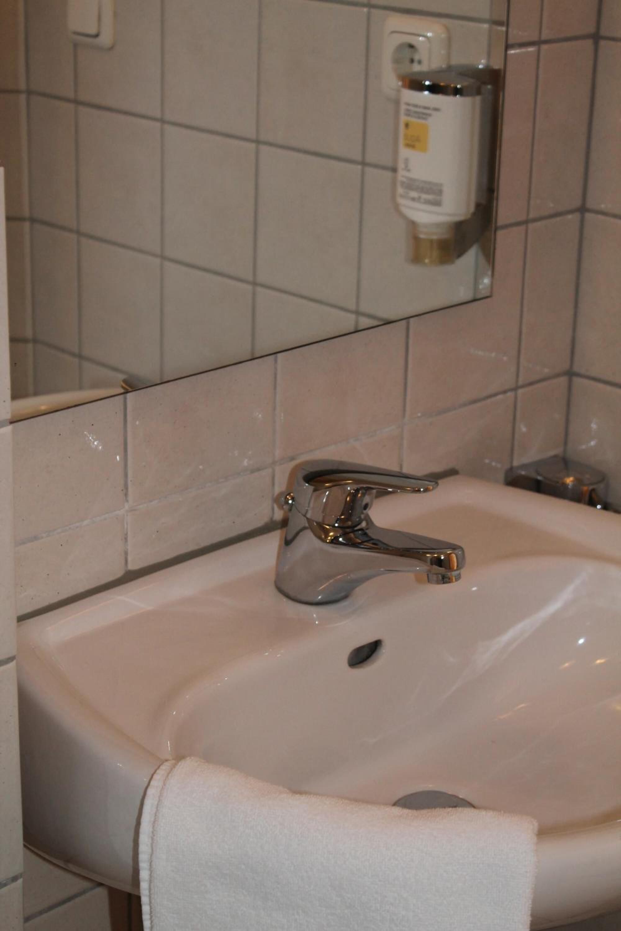Un lavamanos con grifo cromado, una toalla colgada a un lado y un dispensador de jabón en la pared.