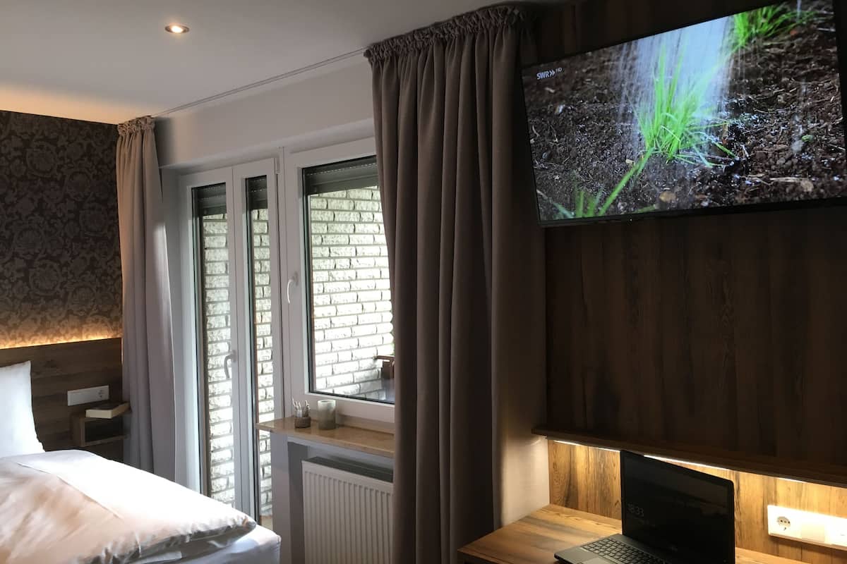 Une chambre d’hôtel avec un lit, un bureau avec un ordinateur portable, un téléviseur fixé au mur et une fenêtre avec des rideaux.