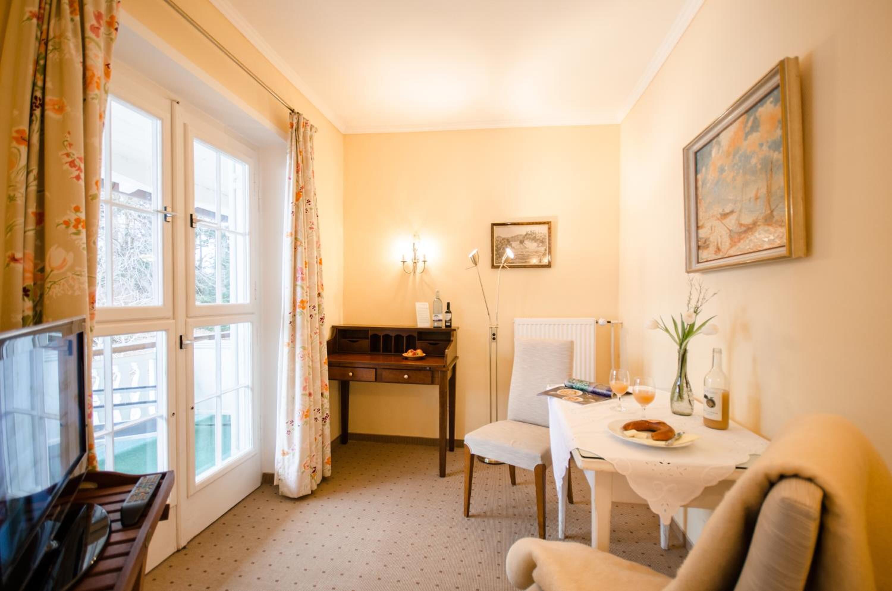 Une pièce chaleureuse avec une table à manger dressée pour deux personnes, une chaise, un bureau avec une lampe et un tableau accroché au mur.