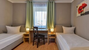 Habitación de hotel con dos camas individuales, una mesita con una silla y un ventanal con cortinas.