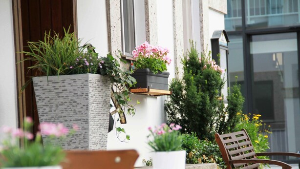 Un patio con un banco de madera, una mesa y varios maceteros con plantas y flores.