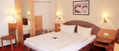 Une chambre d’hôtel avec un grand lit, deux tables de chevet, une chaise, un miroir et un tableau accroché au mur.