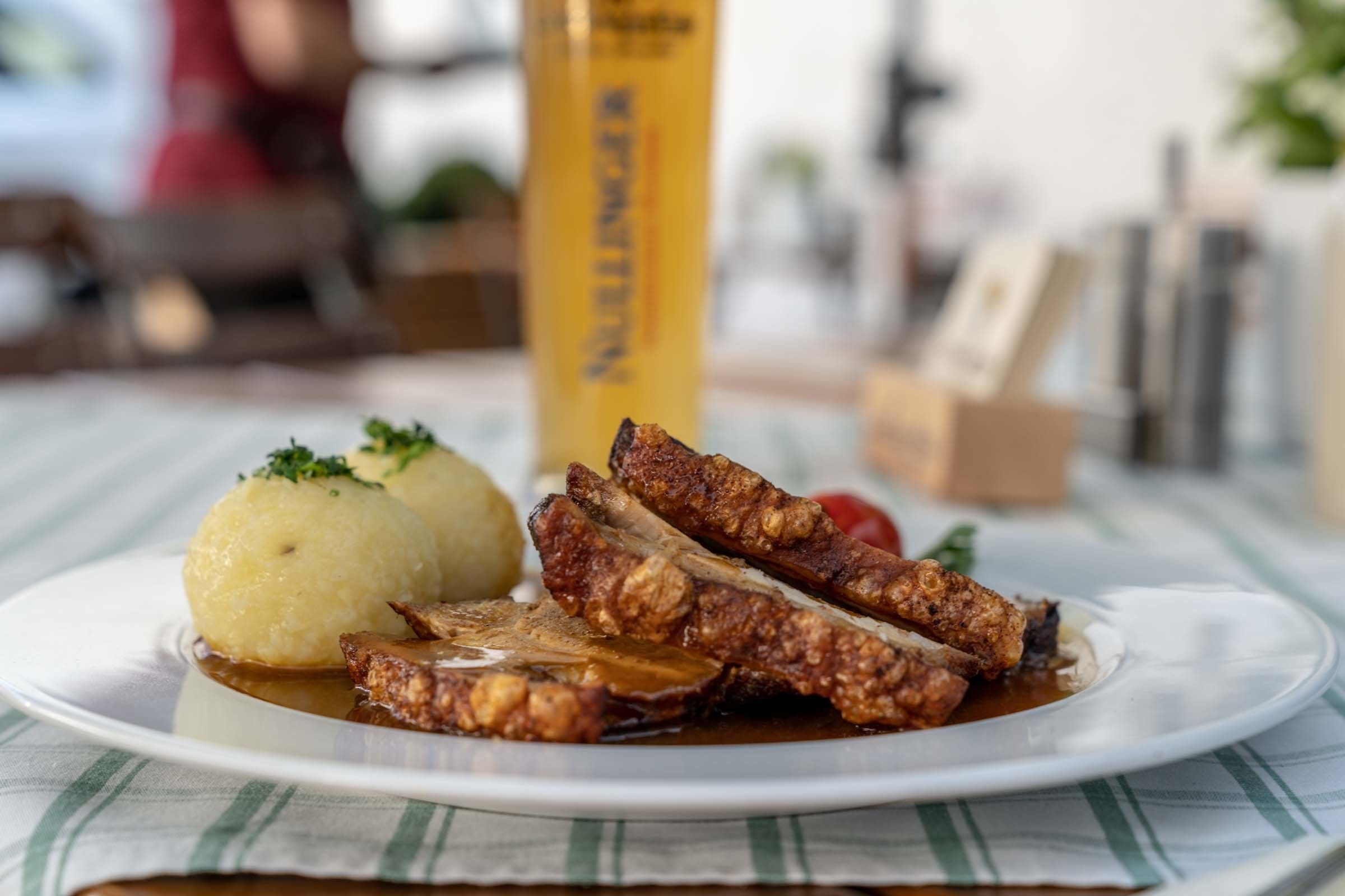A plate with sliced meat and a boiled potato, set on a table with a striped tablecloth.