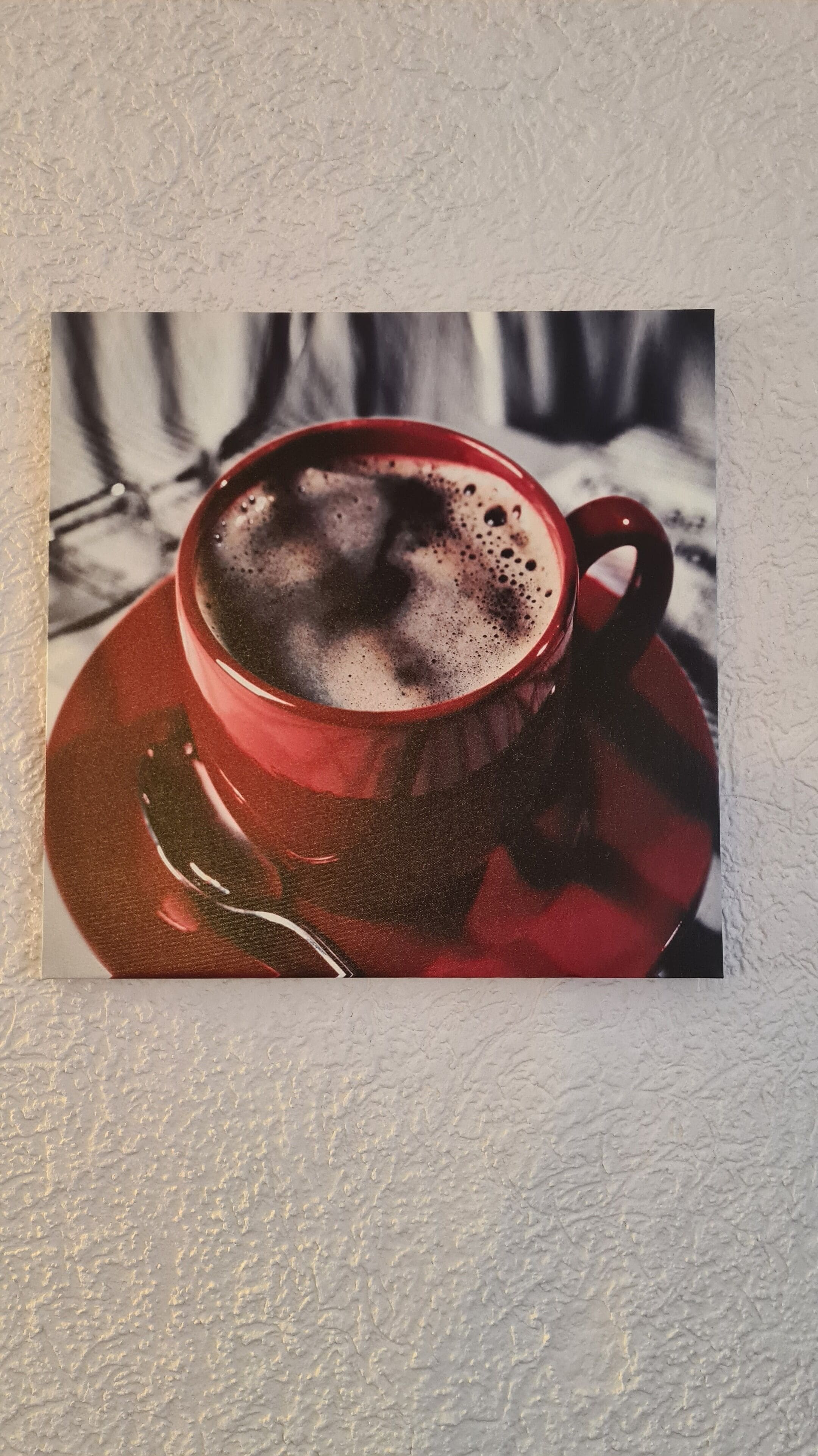 Ein roter Becher mit Untertasse auf einer strukturierten weißen Wand.