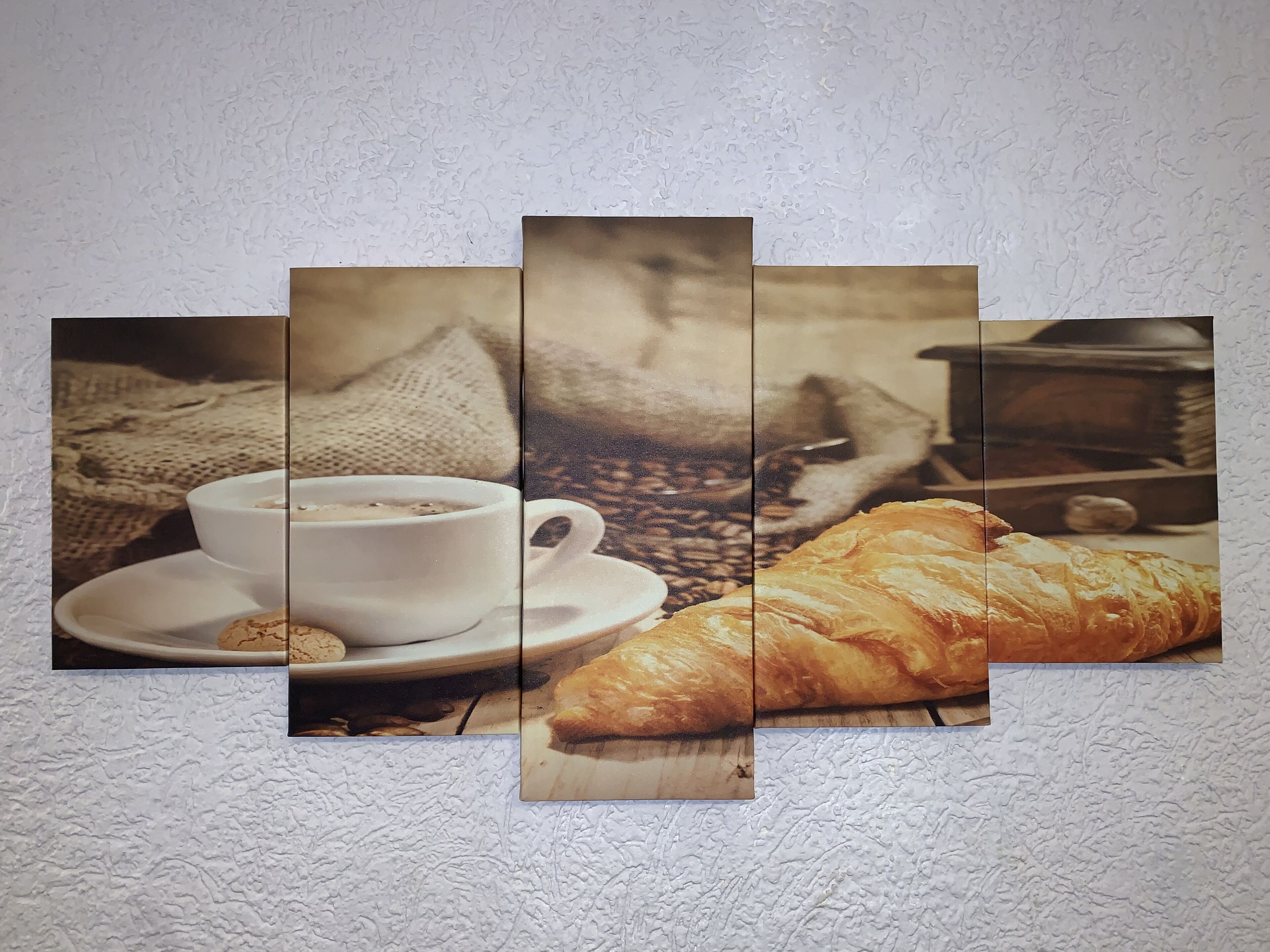 A wall with a three-panel artwork depicting a cup of coffee, a croissant, and a coffee grinder.