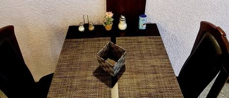 A dining table with a woven placemat, two chairs, a small decorative plant, and a bottle of water.