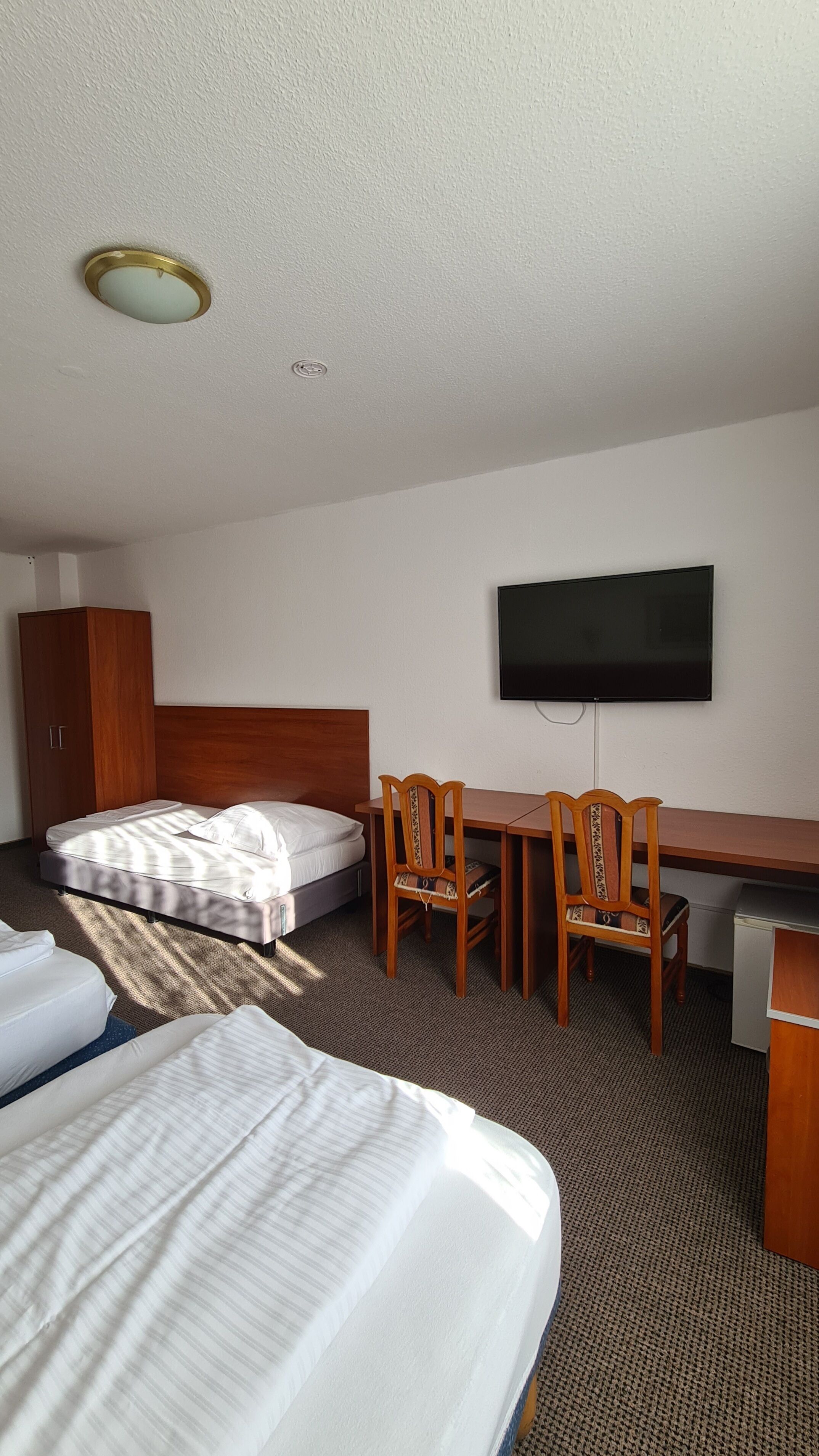 A hotel room with two beds, a desk, two chairs, a television, and a wardrobe.