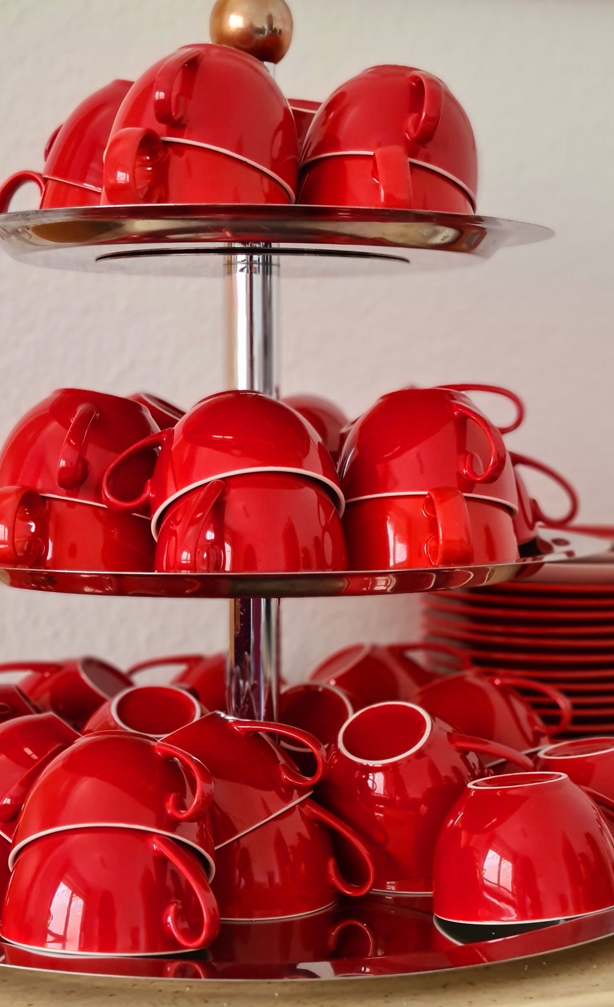 A three-tiered stand with red teacups and saucers.