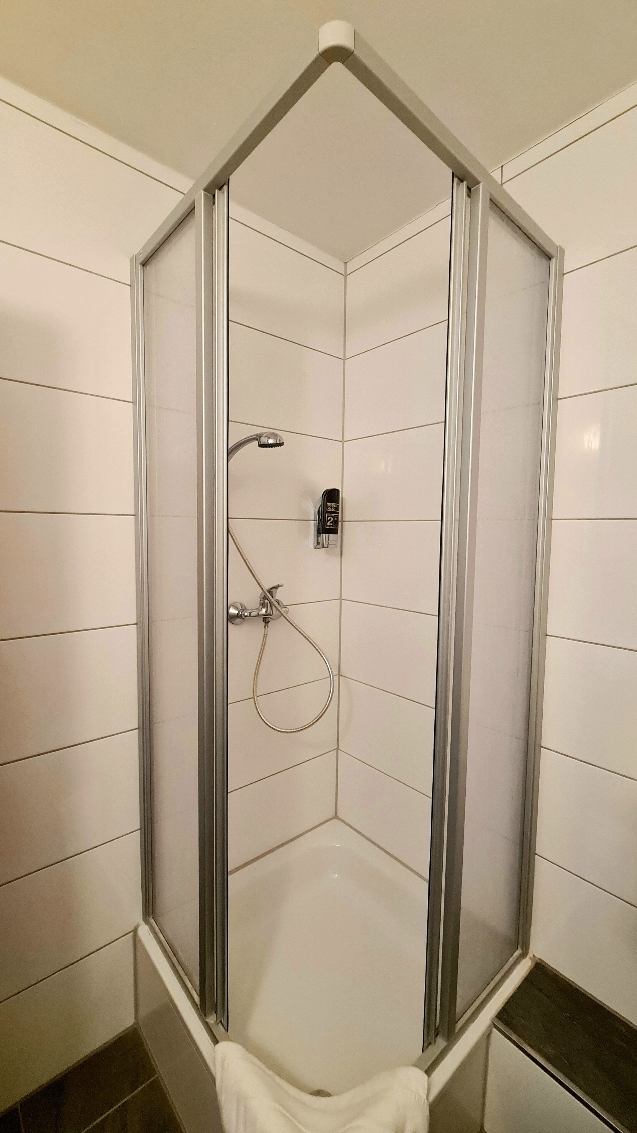 Ducha de esquina con mampara de vidrio, cabezal de ducha manual y panel de control en la pared.