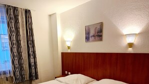 Habitación de hotel con dos camas, cabecero de madera, un cuadro en la pared y dos lámparas fijadas a la pared.