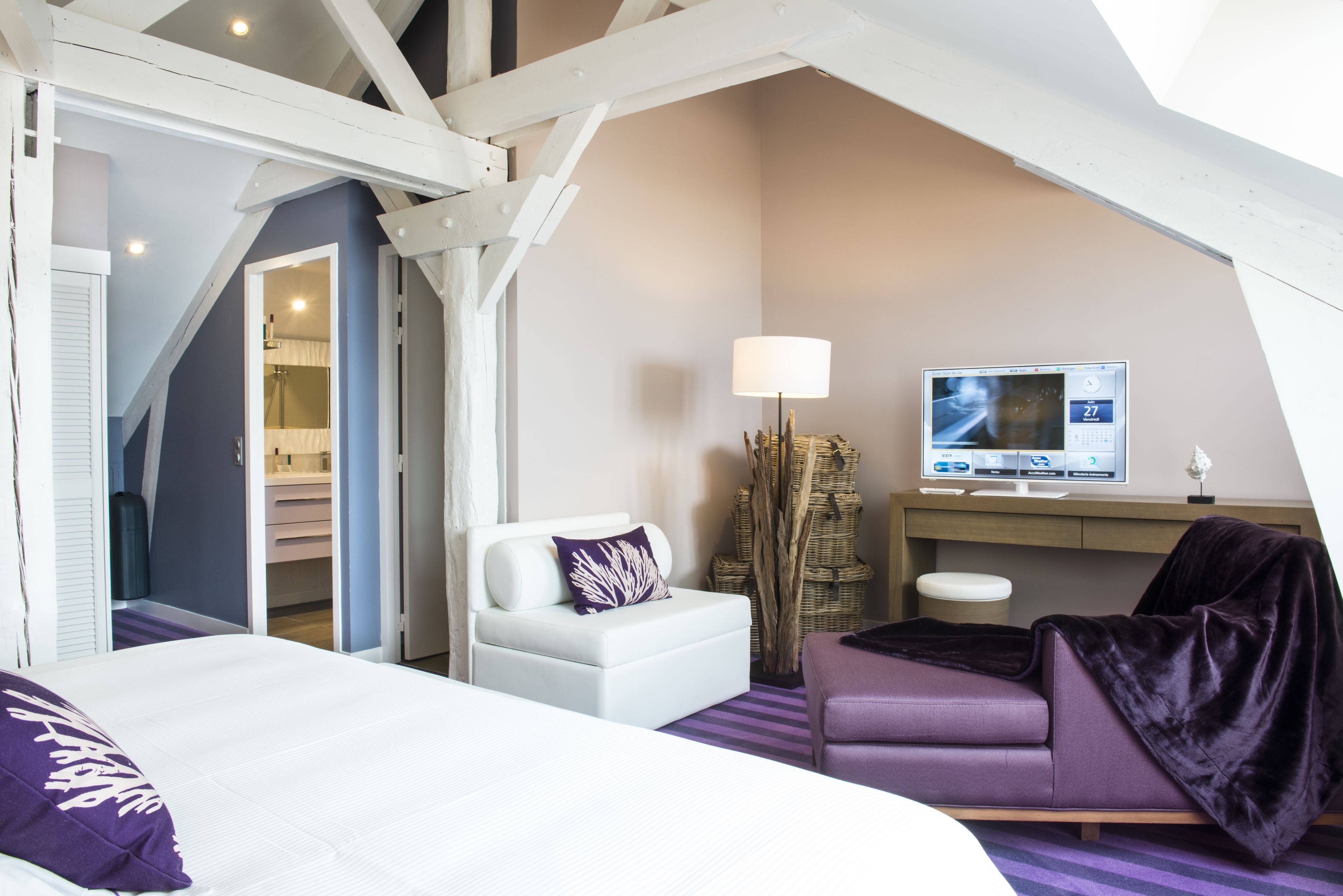 Habitación de hotel con una cama, un sofá blanco, un sillón púrpura, un televisor y un escritorio.
