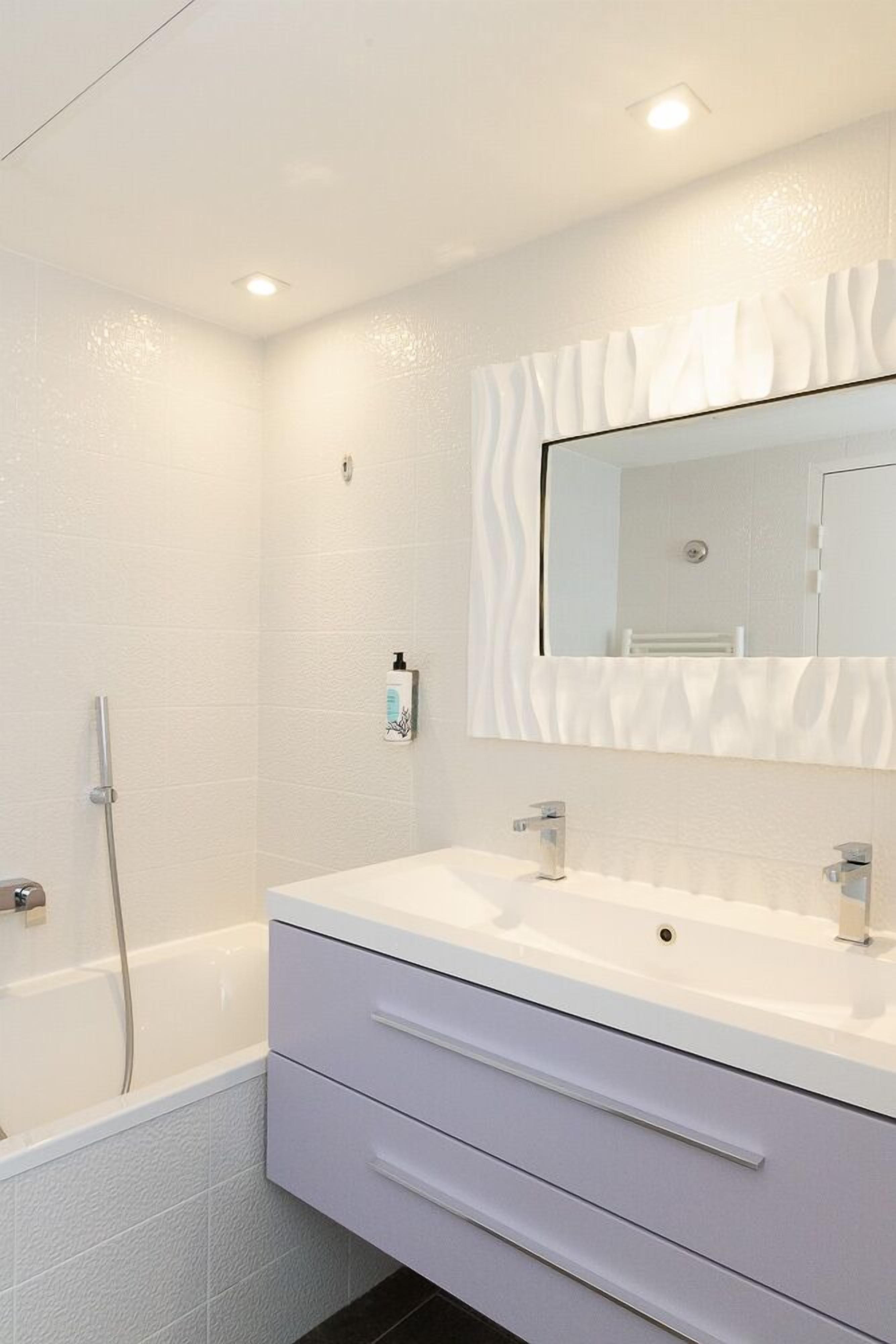 Un baño moderno con tocador blanco, un espejo grande y zona de ducha.