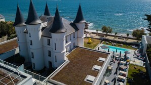 Un edificio al estilo de castillo con múltiples torres, un jardín en la azotea y una zona de piscina con mobiliario exterior.