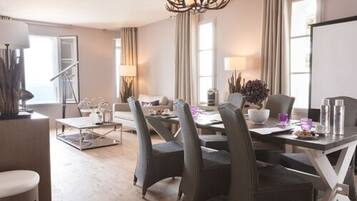 Uma sala de jantar moderna com uma mesa grande, cadeiras e um candelabro. Há um sofá e uma mesinha de centro com objetos decorativos.
