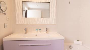 A bathroom with a white vanity, a mirror, a bathtub, and a towel.