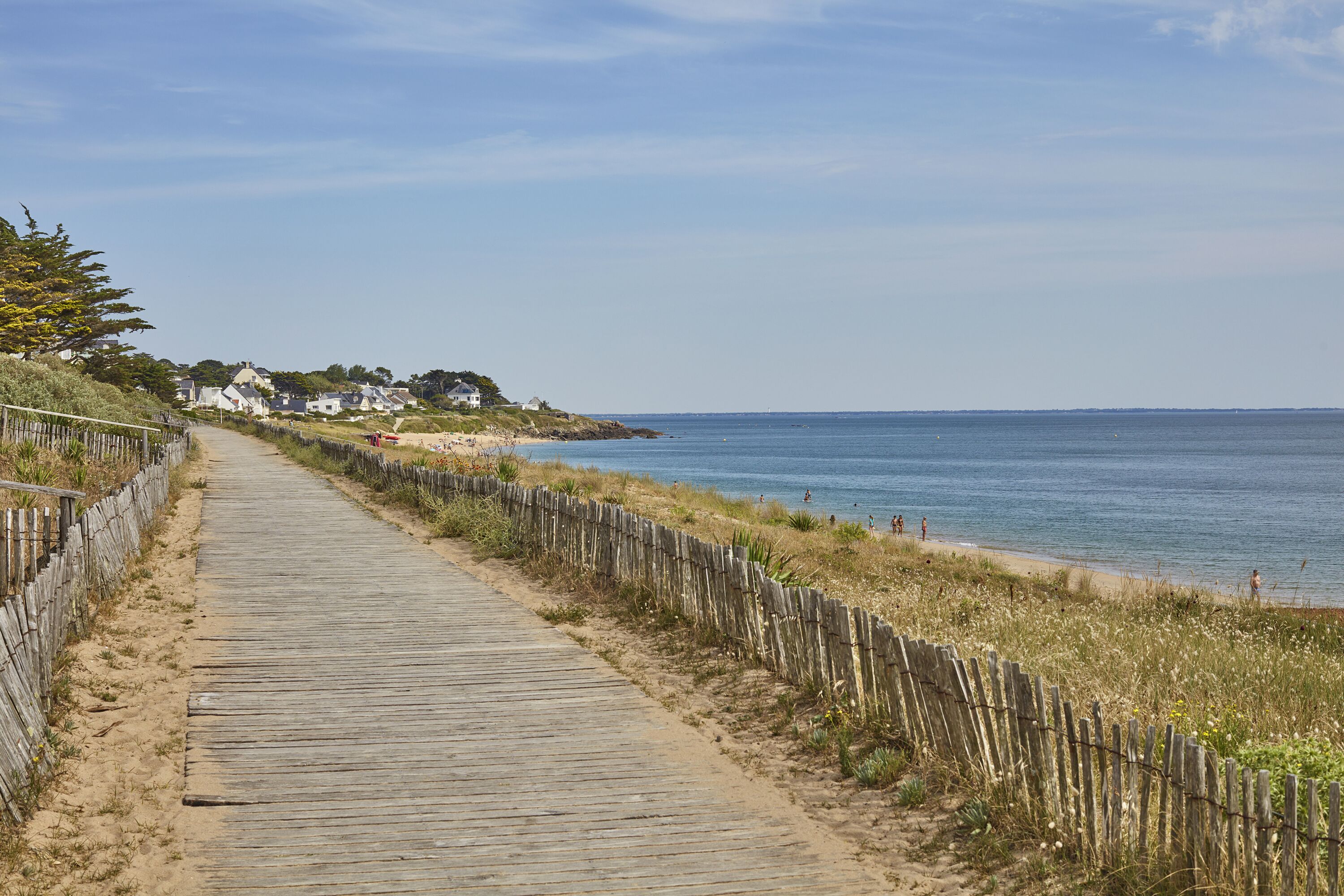 Une promenade en bois menant à une plage, avec des maisons en arrière-plan.