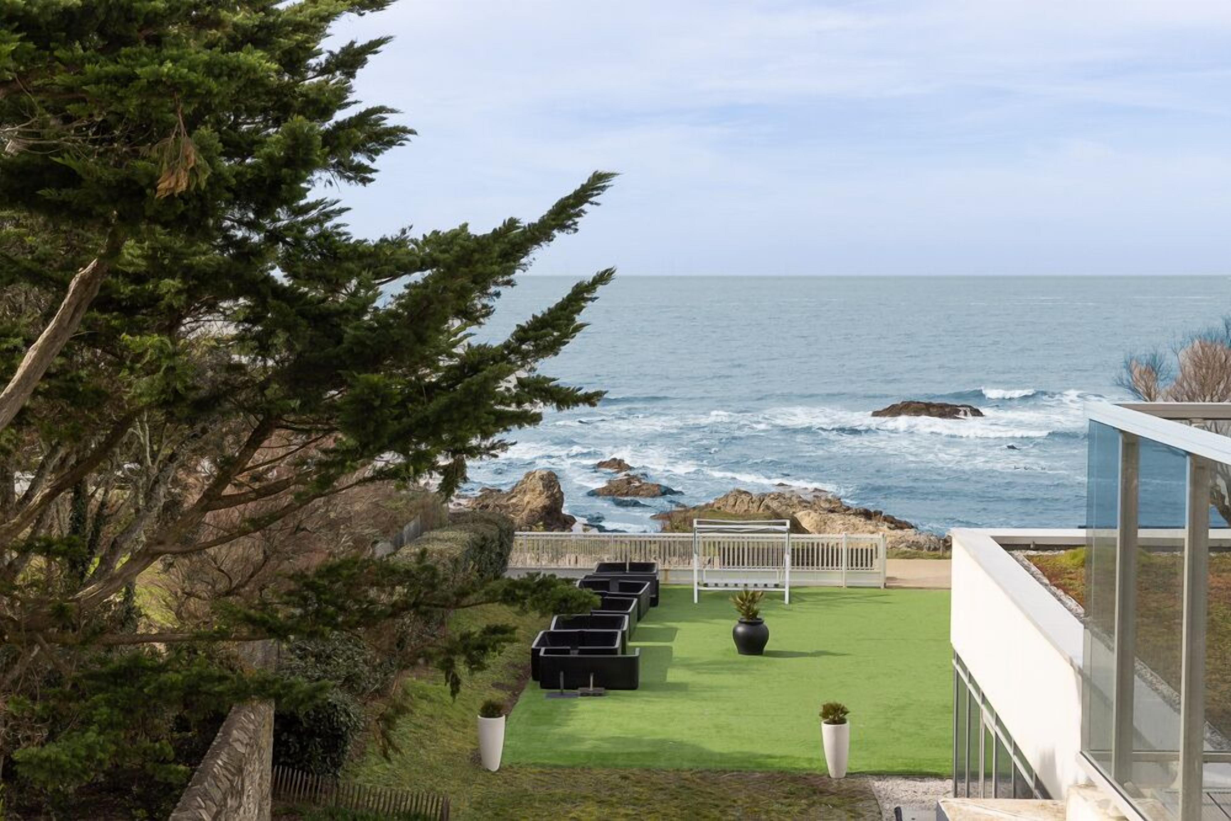 A coastal view with a grassy lawn, outdoor seating, and a modern building with large windows.