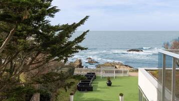 A coastal view with a grassy lawn, outdoor seating, and a modern building with large windows.