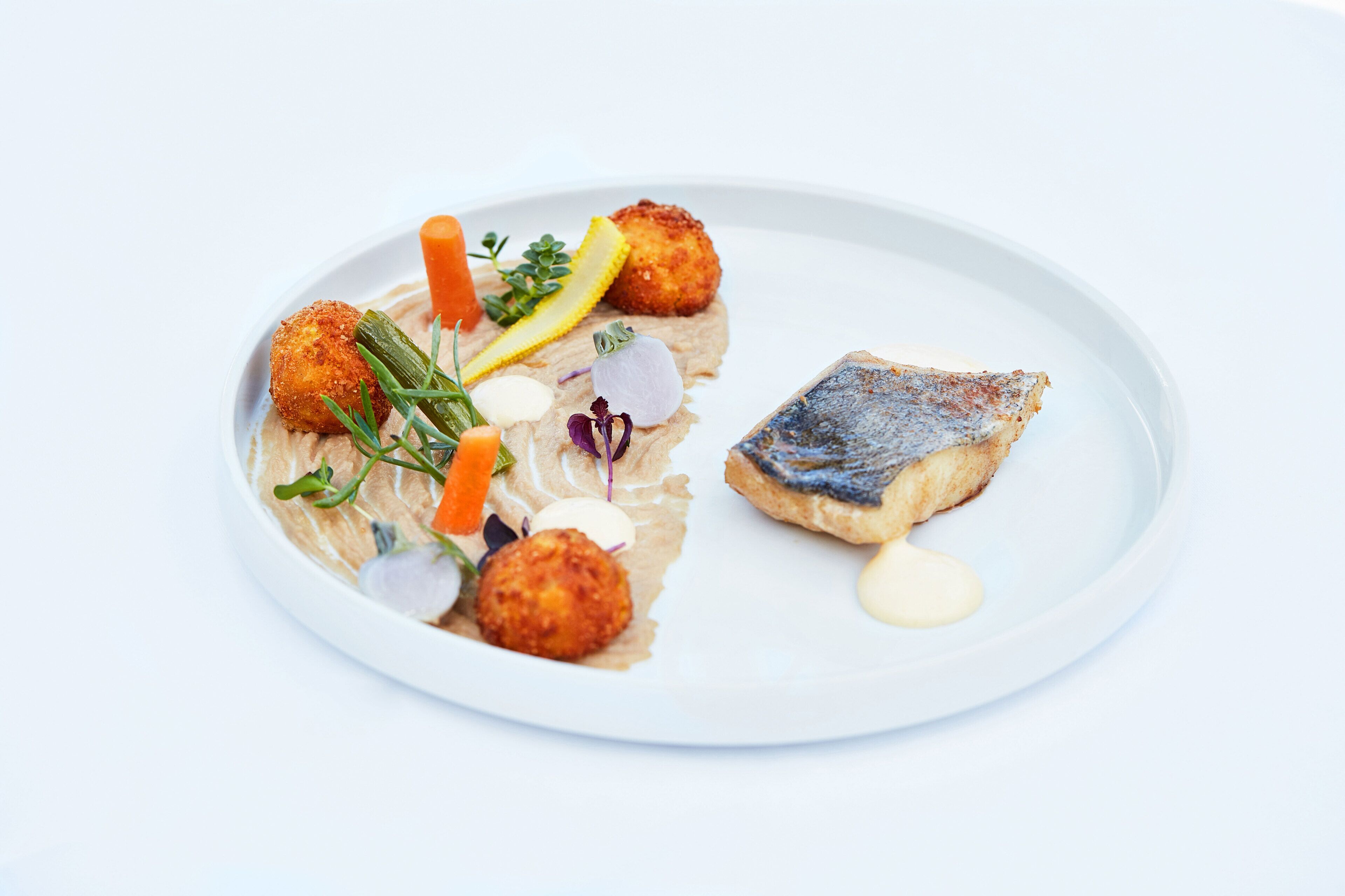 A white plate with a piece of fish, two breaded items, and garnishes.