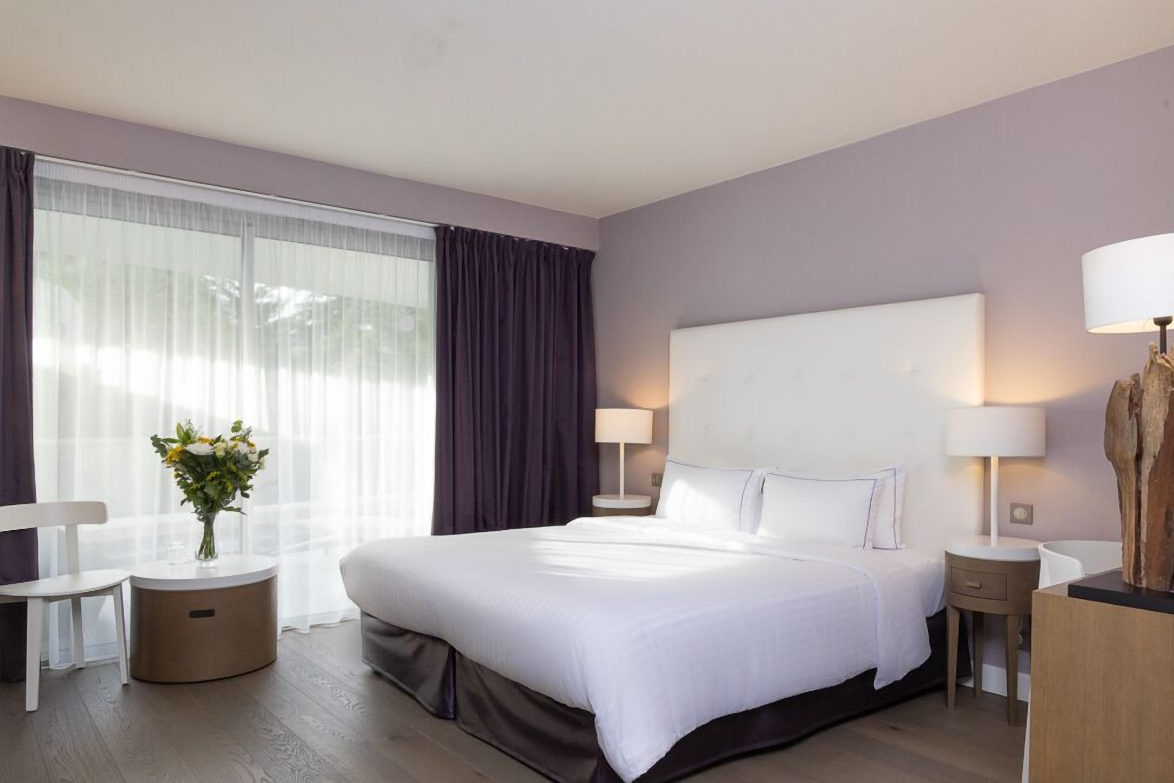 A modern hotel room with a large bed, two bedside tables, a small desk, and a chair.