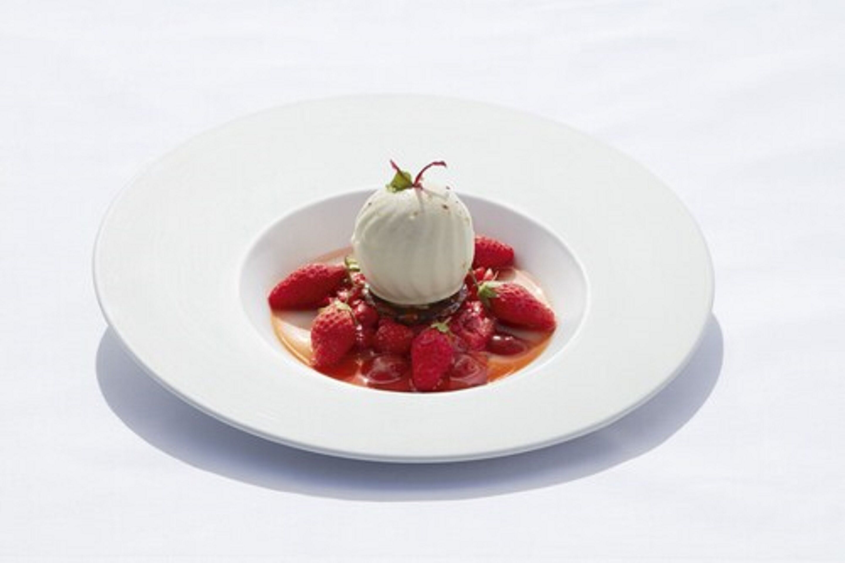 A dessert with a scoop of ice cream on top of strawberries, served on a white plate.