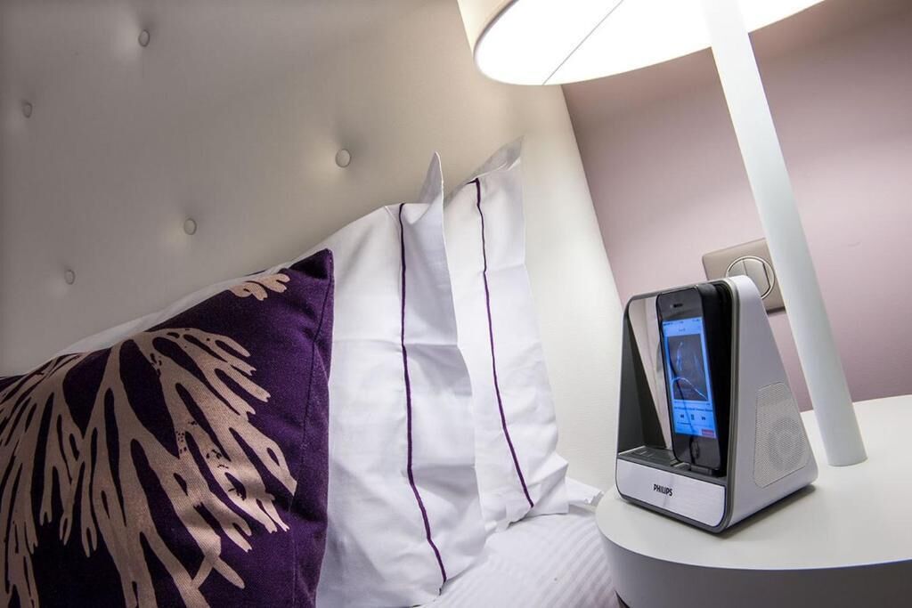 A hotel room with a bed, a pillow, a bedside table, and a Philips phone.