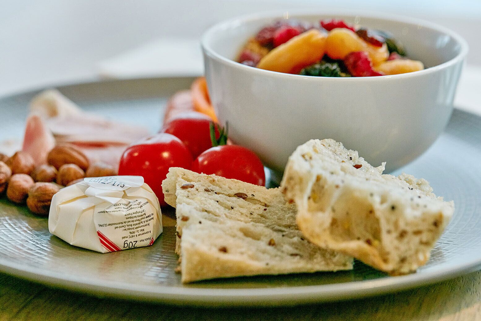 Een bord met een fruitsalade, een sneetje brood, een klein stukje kaas en wat noten.