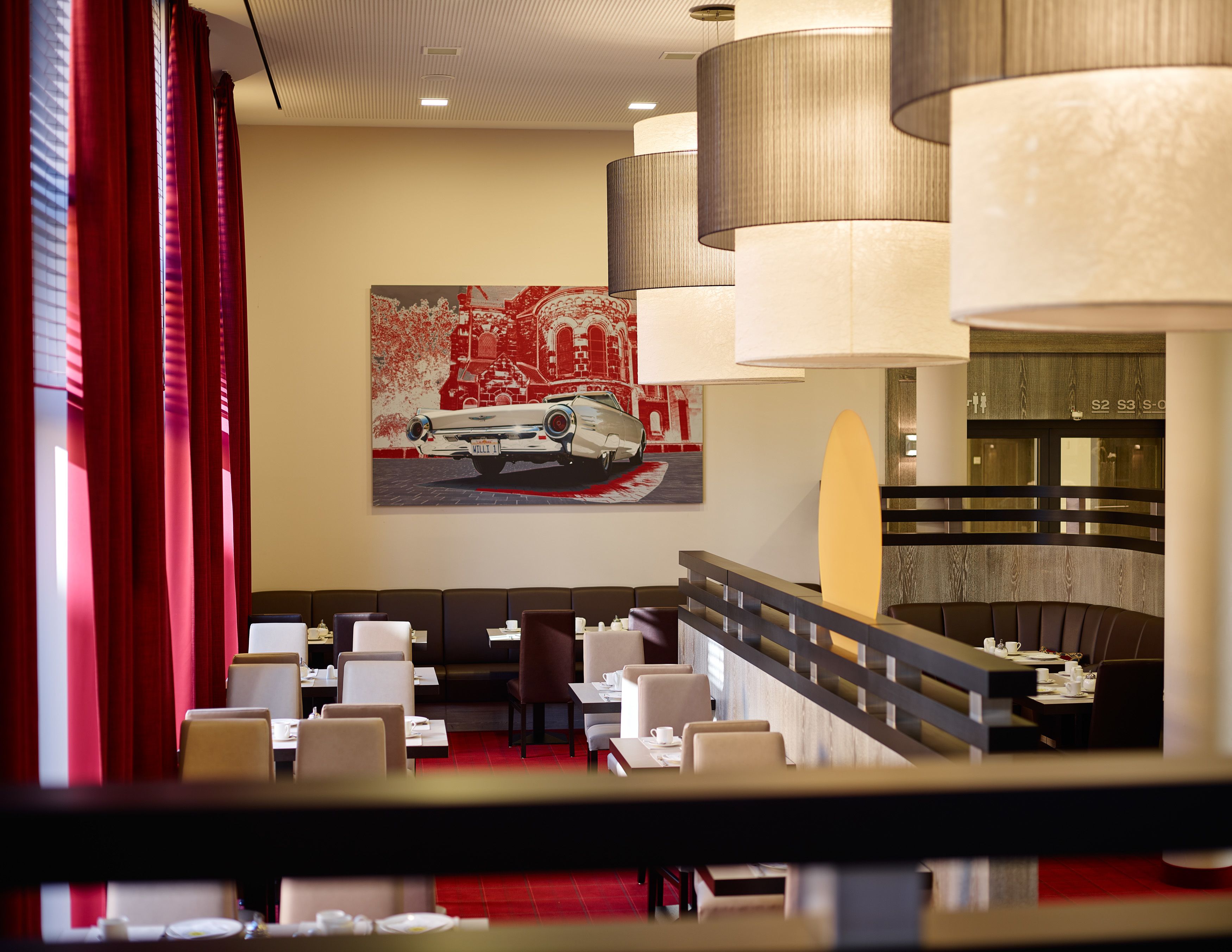 Ein modernes Restaurant mit rotem Teppich, weißen Stühlen und einem großen Gemälde eines Autos an der Wand.