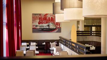 Ein modernes Restaurant mit rotem Teppich, weißen Stühlen und einem großen Gemälde eines Autos an der Wand.