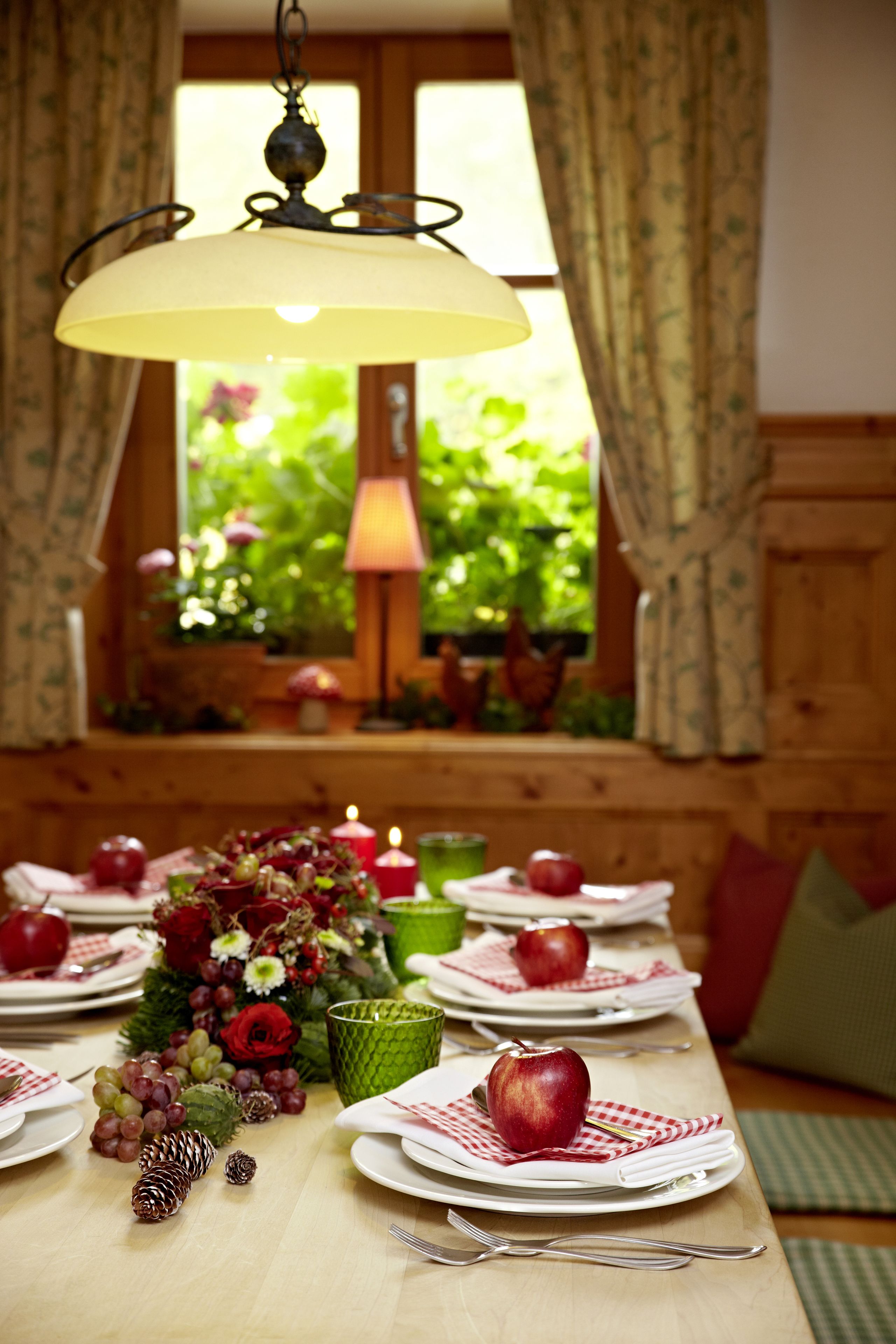Une table à manger dressée avec des assiettes, des couverts et un centre de table composé de fleurs et de fruits.