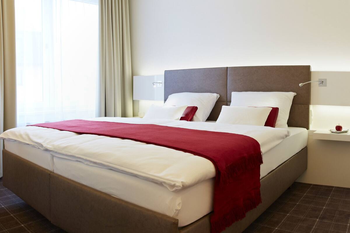 A hotel room with a bed, a nightstand, a lamp, and a window with curtains.