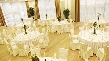 A large, well-lit banquet hall with multiple round tables, each set with white tablecloths and chairs, and floral centerpieces.