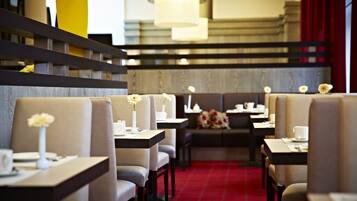A restaurant with booths and tables, each with a vase of flowers, and a red carpeted floor.