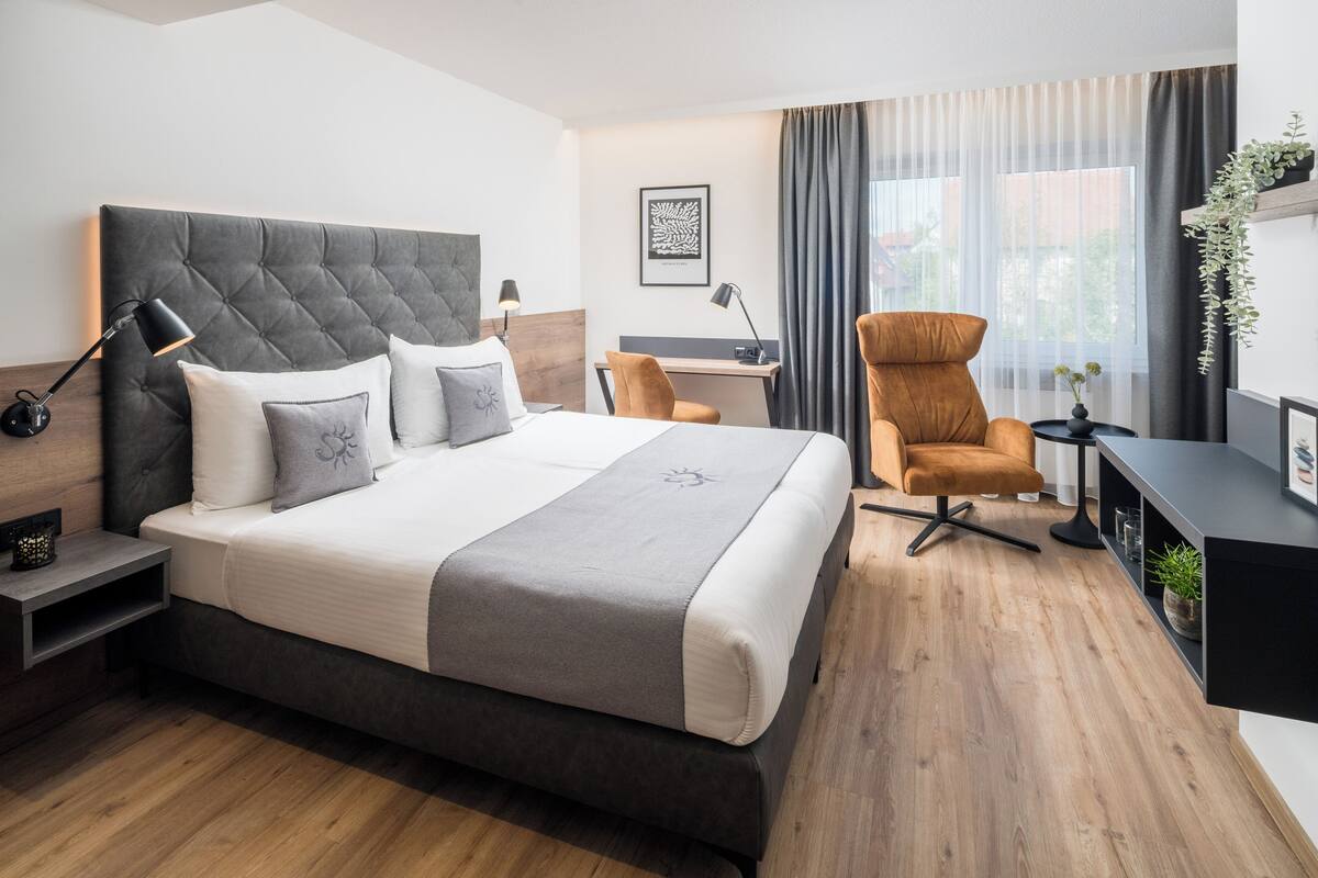 A modern hotel room with a large bed, a desk, a chair, and a small table.