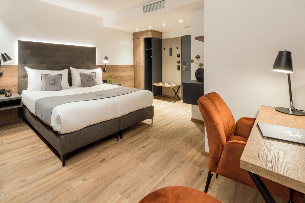 A modern hotel room with a large bed, a desk, and a chair.