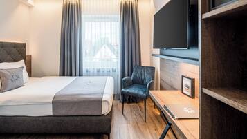 Una habitación de hotel moderna con una cama, una silla, un escritorio con una computadora portátil, un televisor de pantalla plana y una ventana con cortinas.