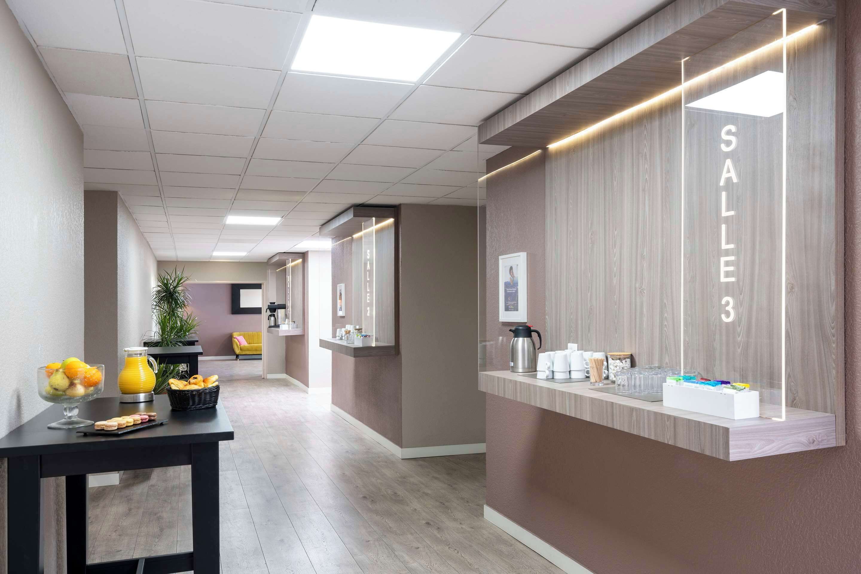 A modern reception area with a counter labeled "SALLE 3," a coffee machine, and a fruit bowl.