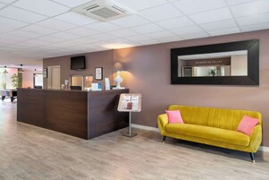 Una zona de recepción con un mostrador de madera, un sofá amarillo, un televisor montado en la pared y un cartel.