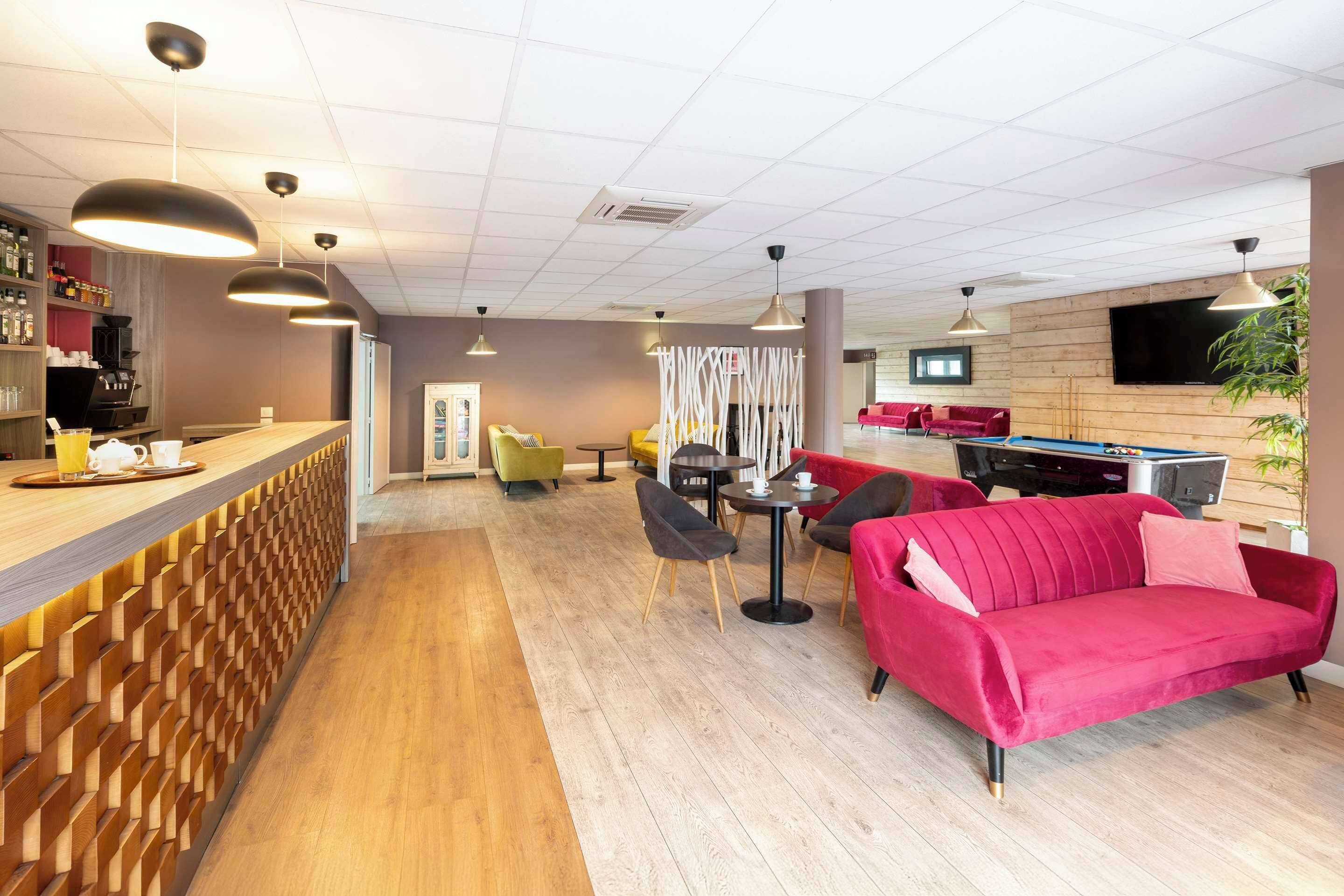 A modern hotel lobby with a wooden reception desk, seating area with a red sofa, and a TV mounted on the wall.
