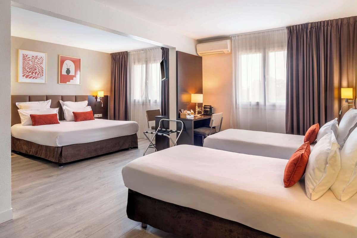 Une chambre d’hôtel avec deux lits, un bureau et une chaise. Elle est équipée de rideaux, de décorations murales et d’un appareil de climatisation.