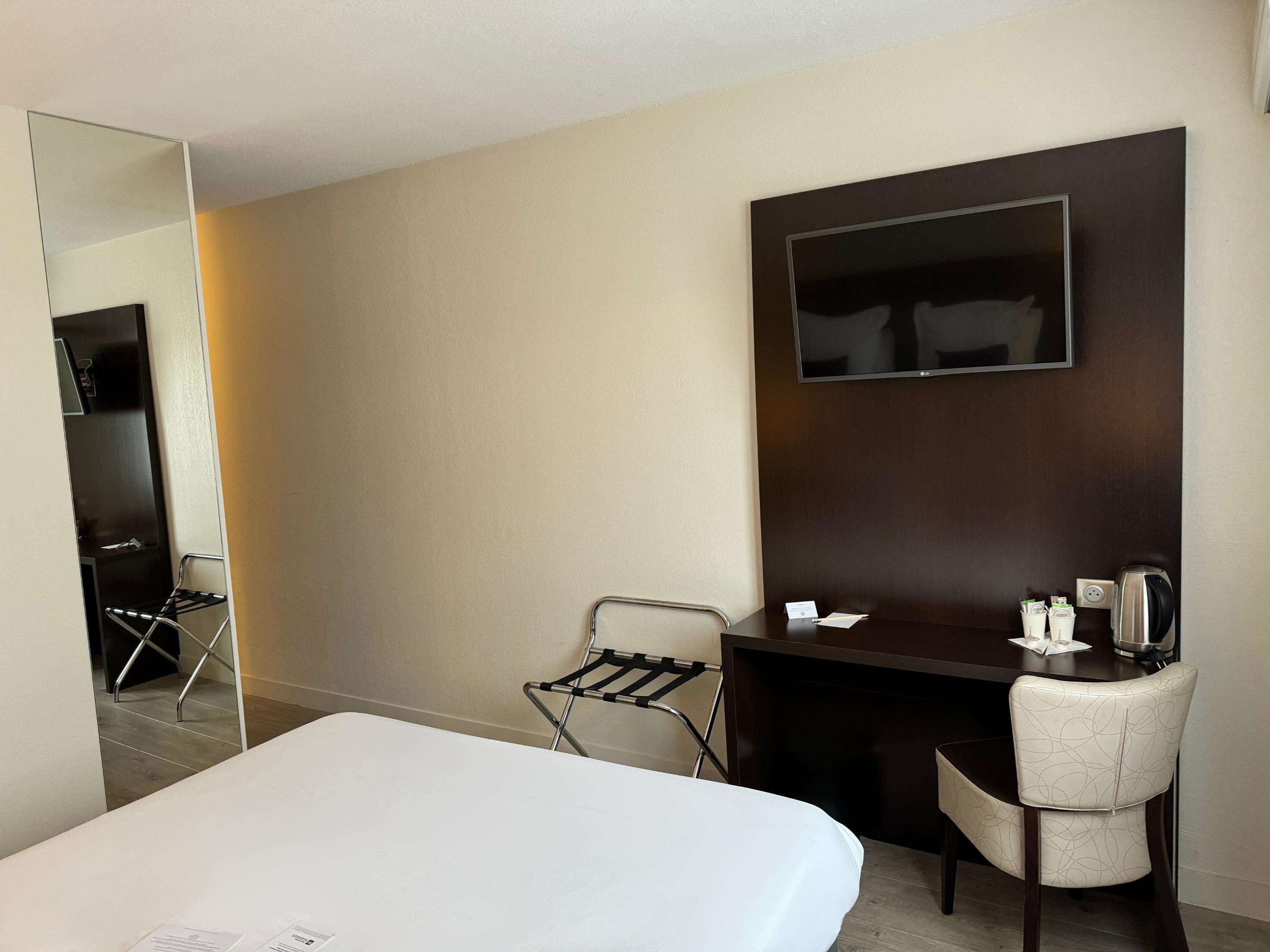 A hotel room with a bed, a desk with a chair, a TV, and a mirror.