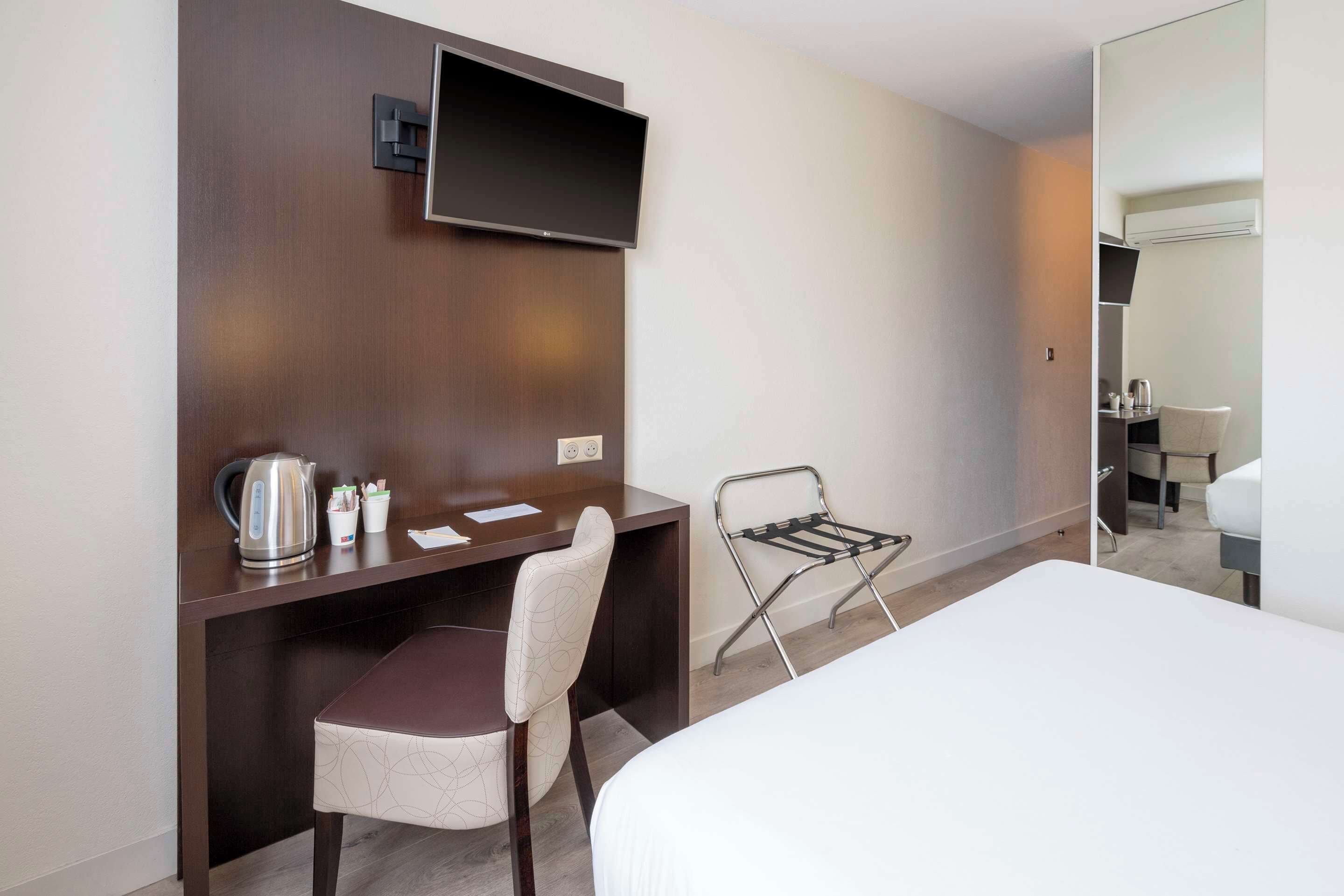 Habitación de hotel con cama, escritorio con silla, televisor montado en la pared y una mesita con hervidor y tazas.